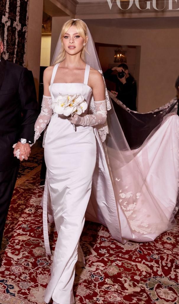 Nicola Peltz in her custom Valentino Couture wedding dress, a sleek square-neck column gown with lace gloves, a cathedral veil, and white orchid bouquet as featured in Vogue