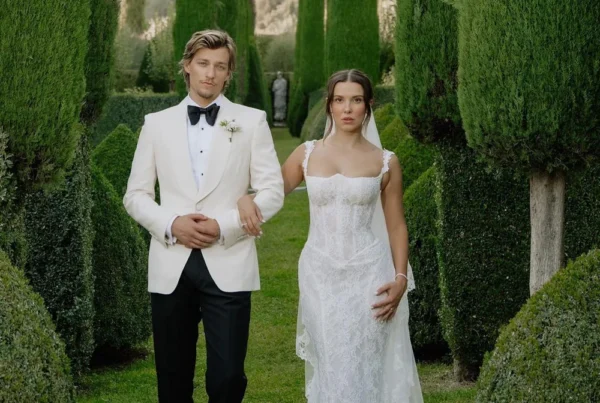 Millie Bobby Brown and Jake Bongiovi on their wedding day, with Millie wearing a fitted Galia Lahav lace gown with lace-trimmed straps and a cathedral veil, surrounded by tall cypress trees