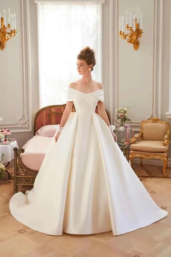 Off-the-shoulder twisted bodice satin ball gown wedding dress in an ornate French-inspired interior at La Mariée Boutique Tulsa