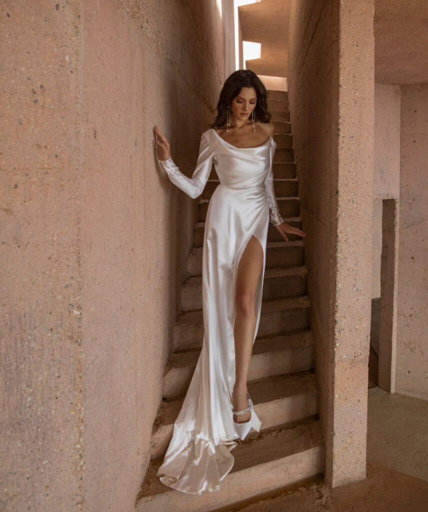 Asymmetric one-shoulder satin wedding gown with long sleeve and thigh-high slit at La Mariée Boutique Tulsa