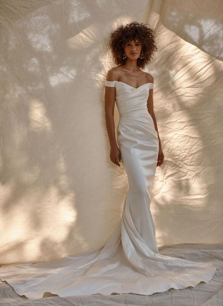 Off-the-shoulder ruched satin mermaid wedding gown with a sweetheart neckline and cathedral train at La Mariée Boutique Tulsa
