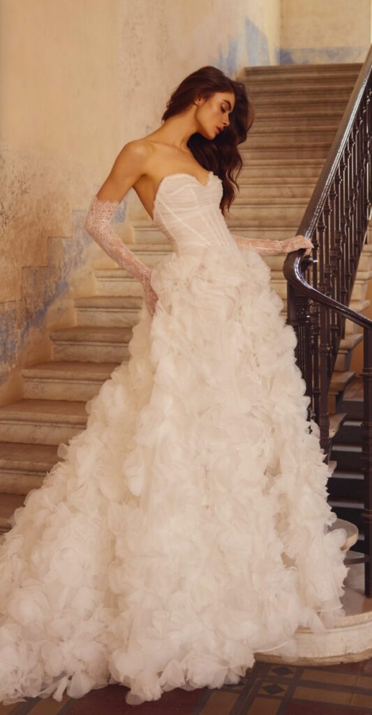 Strapless sweetheart ball gown wedding dress with a dimensional ruffled petal skirt and sheer lace gloves at La Mariée Boutique Tulsa