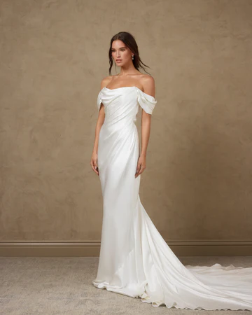 Draped off-the-shoulder satin mermaid wedding gown with a cowl neckline and sweep train at La Mariée Boutique Tulsa