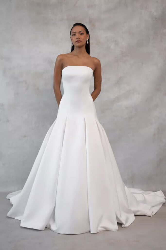 Minimalist strapless straight-neck satin ball gown wedding dress with pleated skirt and cathedral train at La Mariée Boutique Tulsa