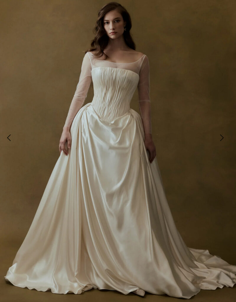 Sheer long-sleeve ball gown wedding dress with a ruched corset bodice and full draped satin skirt at La Mariée Boutique Tulsa