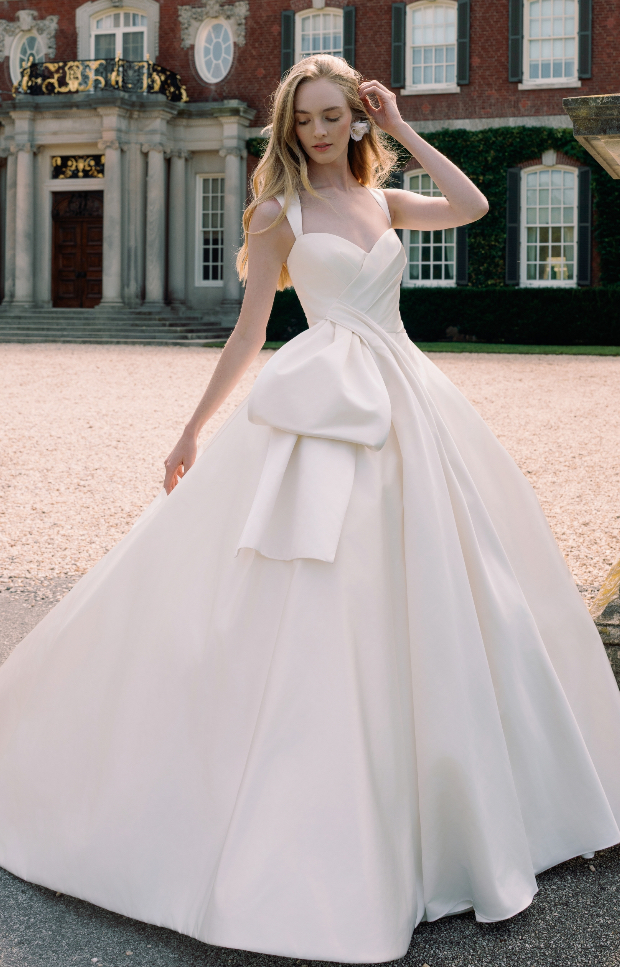 Sweetheart strap satin ball gown wedding dress with an oversized bow at the waist in front of a grand estate at La Mariée Boutique Tulsa