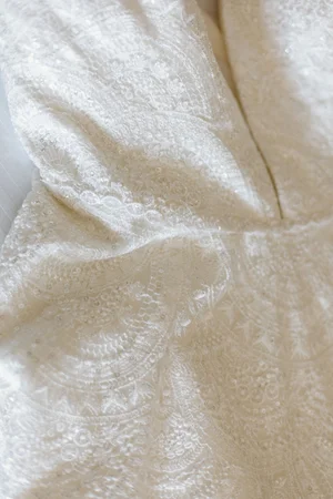Close-up detail of the bride's lace wedding gown showing intricate floral and mandala lace pattern with a deep V-neckline