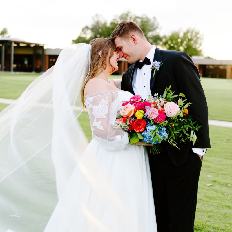 Bride and groom in golden hour wedding portrait with flowing cathedral veil and vibrant garden bouquet at Tulsa Country Club
