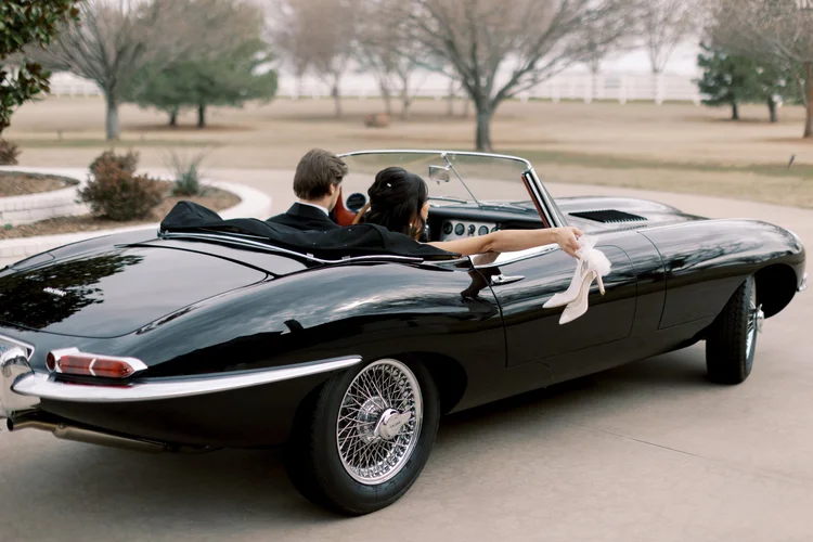 Bride and groom riding in a classic black convertible sports car, bride's Bella Belle bridal heels dangling out the window