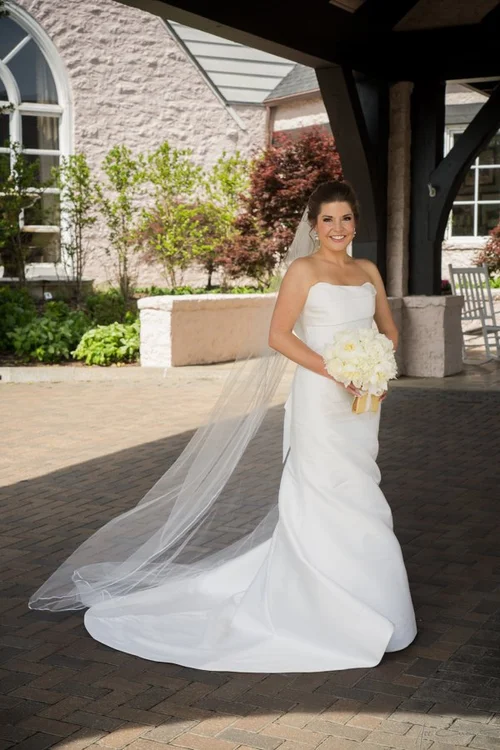 Bride and groom sharing their first kiss at the altar of St. John's Episcopal Church, bride in a strapless satin mermaid gown with cathedral veil, soft pastel floral arrangements in the background
