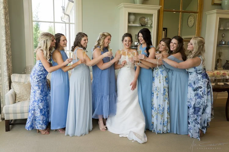 Bride toasting with her bridesmaids while getting ready before the wedding ceremony, bridesmaids wearing mix-and-match blue floral and solid maxi dresses