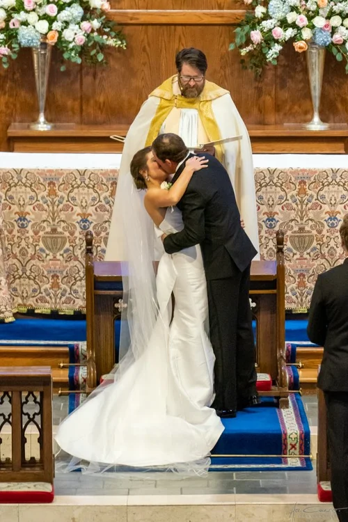 Black and white aerial view of bride walking down the aisle at St. John's Episcopal Church in Tulsa, full congregation standing, cathedral veil trailing behind her strapless satin gown