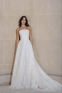 Graham is an arched strapless ball gown crafted in silk white corded lace, highlighted by a Chantilly lace underlay. The layered lace construction adds depth and texture throughout the full skirt, while a scalloped hem provides a defined, delicate finish. The structured ball gown silhouette balances intricate lace detail with clean, classic shape.