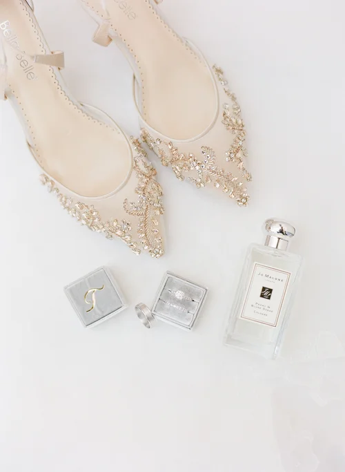 Bridal detail flat lay featuring Bella Belle Frances pointed-toe heels with gold beaded embroidery, diamond engagement ring, monogram ring box, and Jo Malone perfume