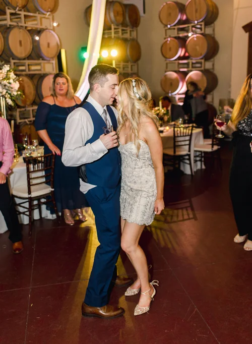 Bride in a beaded short reception dress dancing with her groom in a winery reception venue, wearing Bella Belle Frances embellished flats